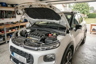 Moteur 1.2 PureTech du Citroën C3 Aircross ouvert dans un garage résidentiel, montrant les composants du compartiment moteur avec signes d'usure réalistes