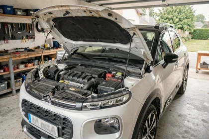 Moteur 1.2 PureTech du Citroën C3 Aircross ouvert dans un garage résidentiel, montrant les composants du compartiment moteur avec signes d'usure réalistes